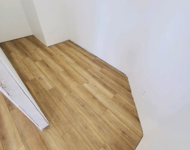Newly installed light brown laminate wood flooring in an angled hallway, next to white walls and baseboards.